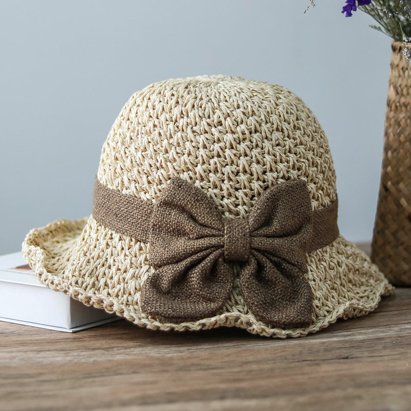 Vintage Foldable Straw Sun Hat with Wide Brim Bow on wooden surface, showcasing its elegant design and brown bow accent.
